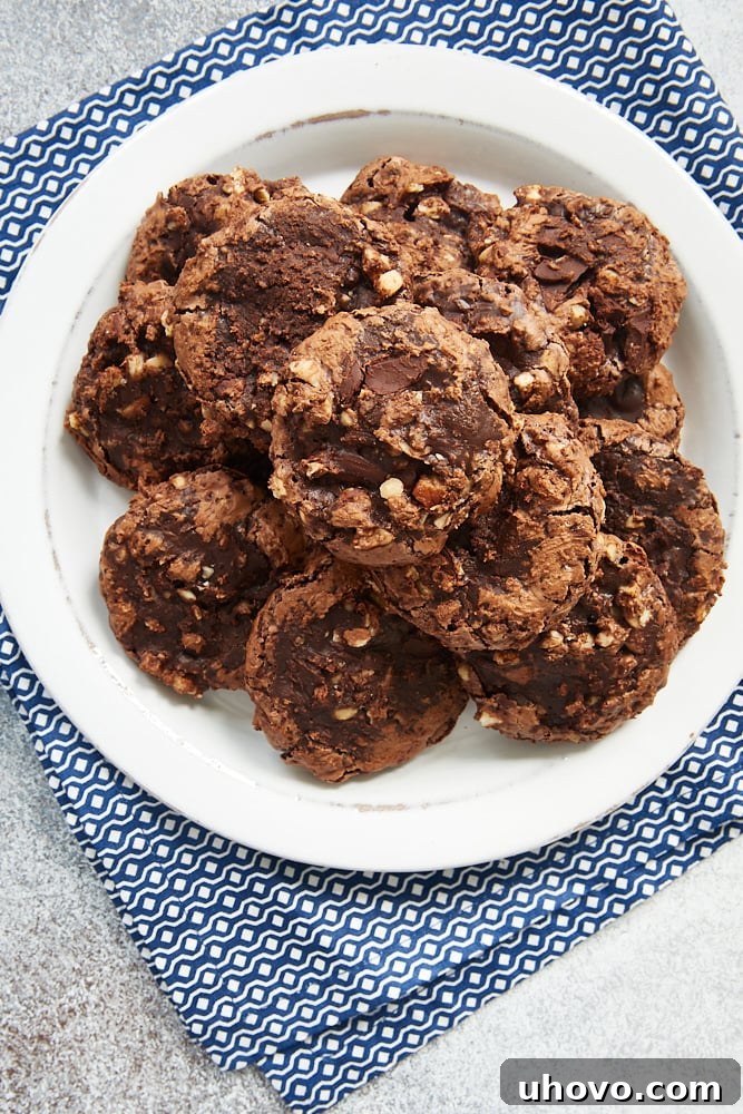 Overhead view of Flourless Chocolate Hazelnut Cookies on a white plate on a blue and white napkin, showing the beautiful crackle tops.