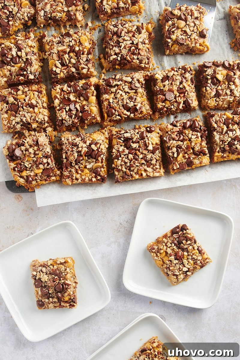 Seven layer bars with chocolate, coconut, and nuts, arranged on parchment paper and white square plates, ready for serving.