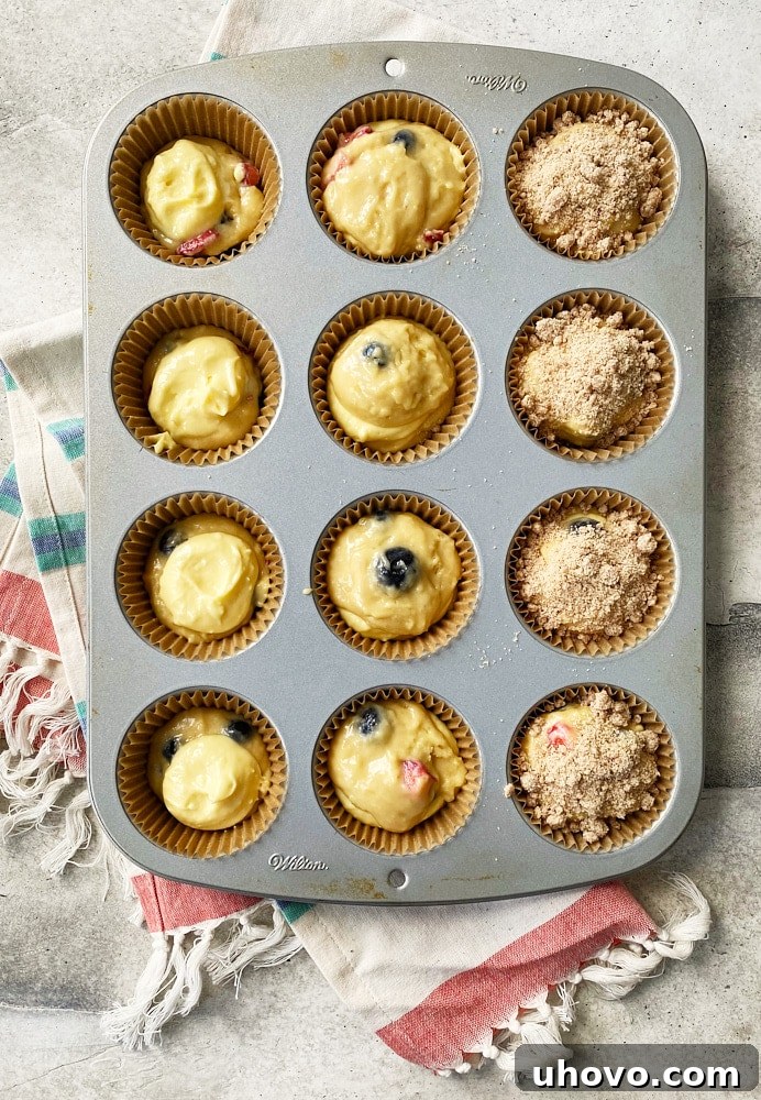 Overhead shot of Berry Cheesecake Muffin batter being scooped into a muffin pan, showing the rich texture and readiness for the oven.