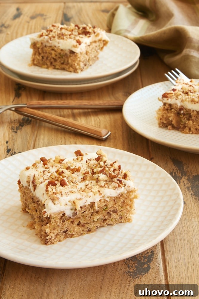 Delightful Frosted Zucchini Bars generously topped with cream cheese frosting and sprinkled nuts, served on elegant white and beige plates.