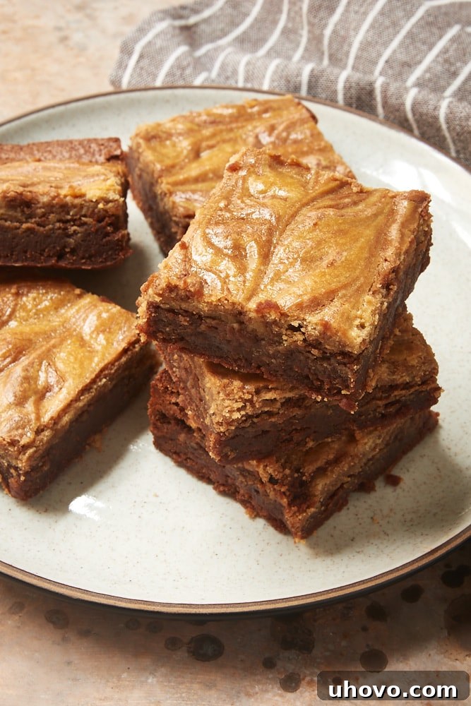 Multiple Cookie Butter Cheesecake Brownies stacked on a white and brown speckled plate, highlighting their height and layered composition.