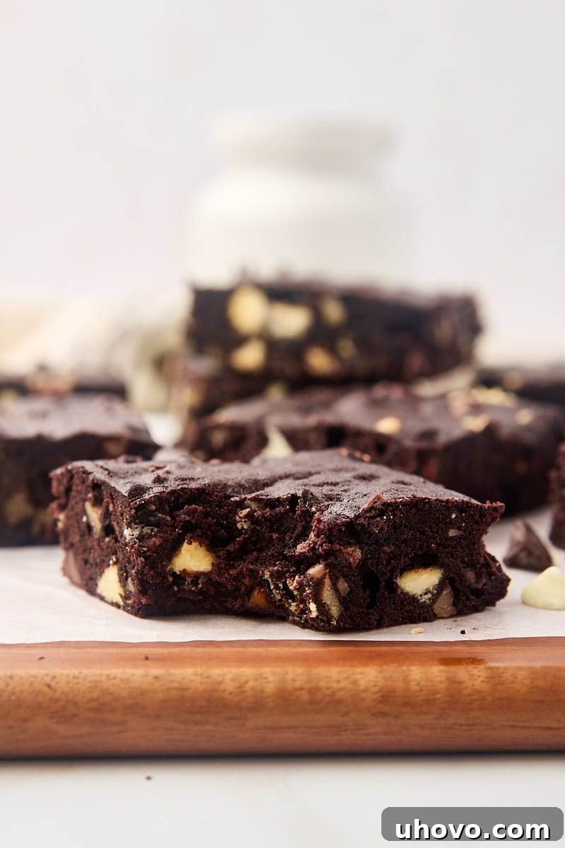 A perfectly fudgy triple chocolate brownie with a bite taken out, resting on a cutting board