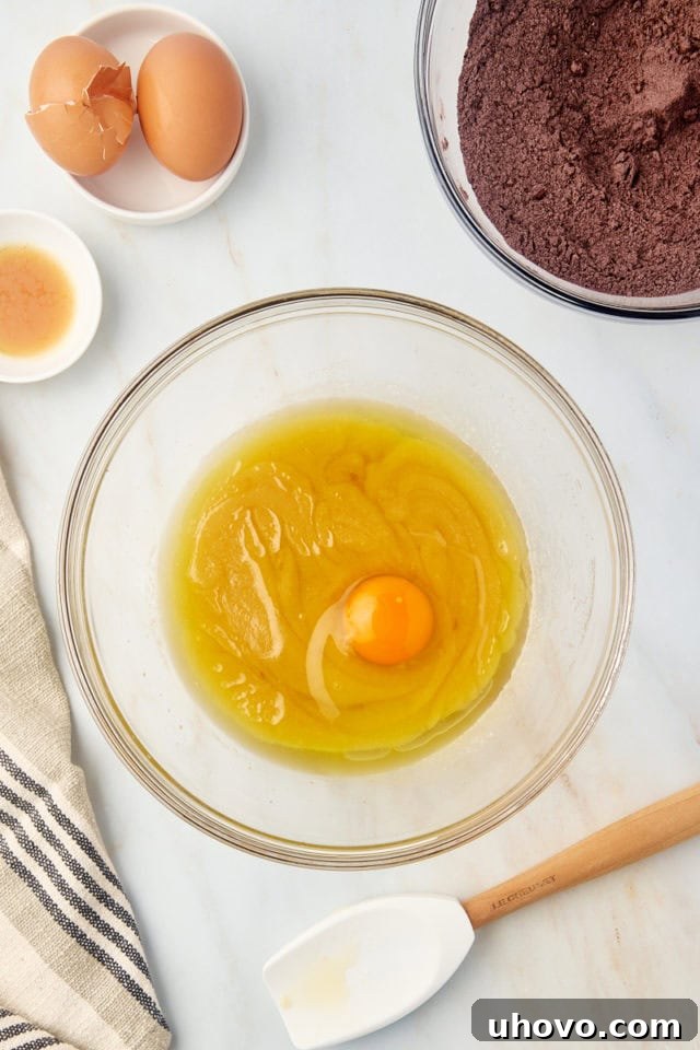 Egg being added to wet ingredients in a mixing bowl for brownie batter