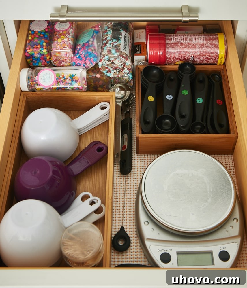 A kitchen drawer with neatly organized baking tools using dividers, including multiple sets of measuring spoons and spatulas.
