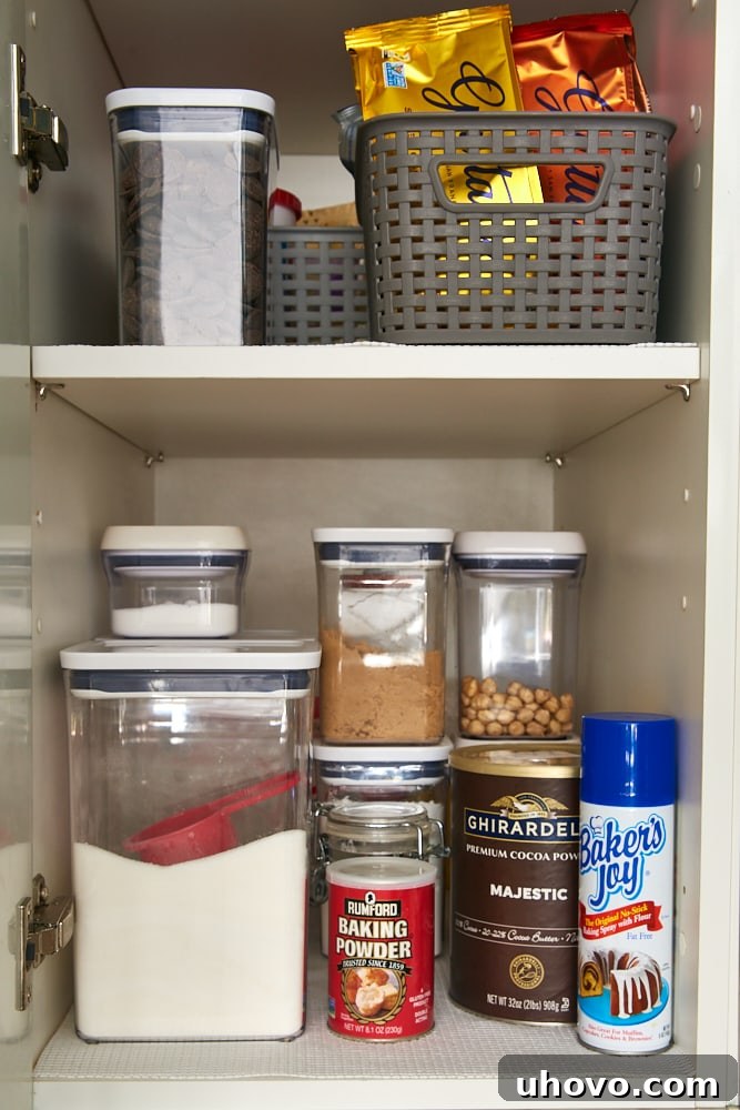 A well-organized kitchen cabinet with baking ingredients in clear, labeled containers and bins.