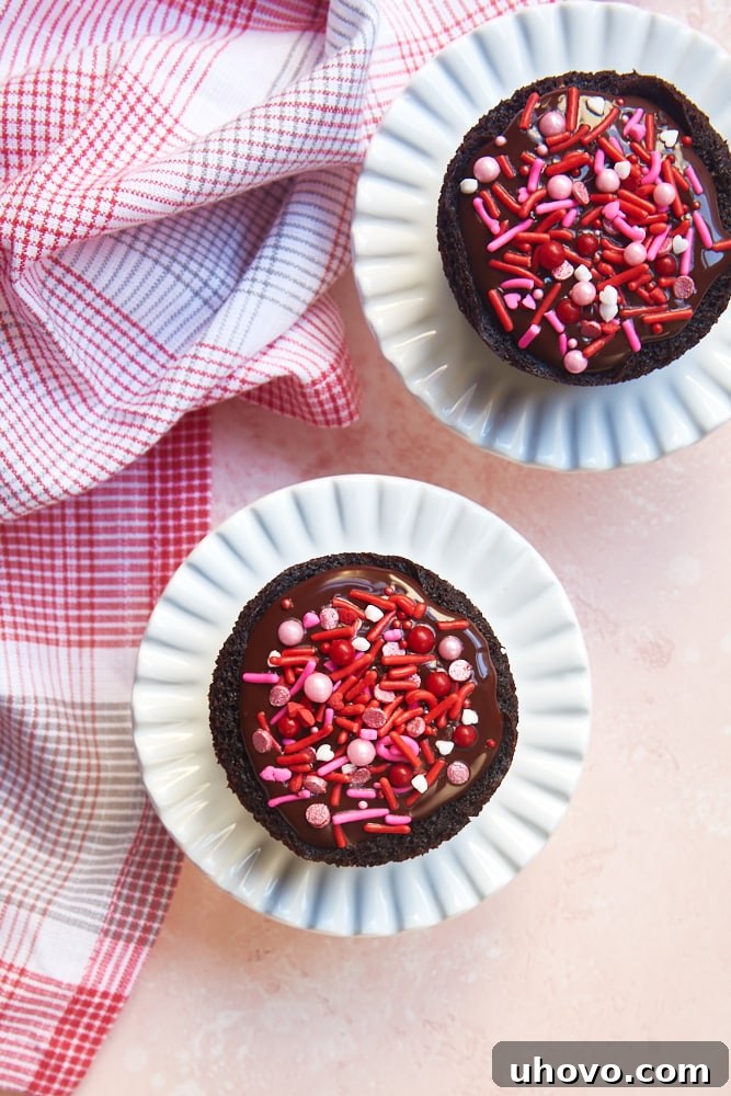 Overhead view of two Chocolate Cupcakes for Two on elegant small white cake stands, showcasing their rich melted chocolate topping and festive sprinkles