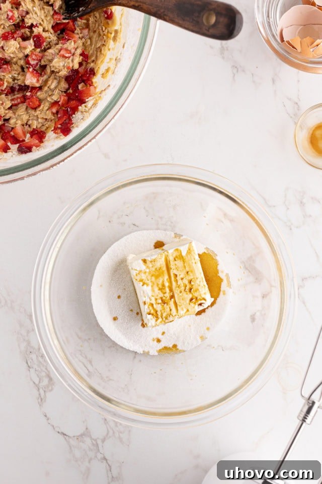 Overhead view of softened cream cheese, granulated sugar, and vanilla extract placed together in a glass mixing bowl, ready to be blended for the swirl.