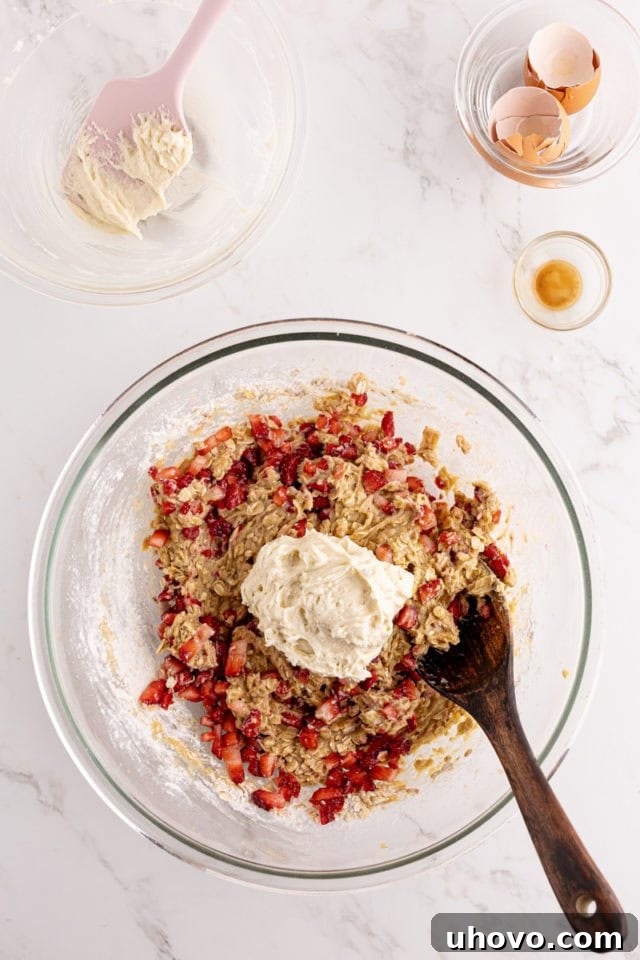 Overhead view of spoonfuls of the smooth cream cheese mixture being strategically added to the strawberry bread batter in a glass mixing bowl.