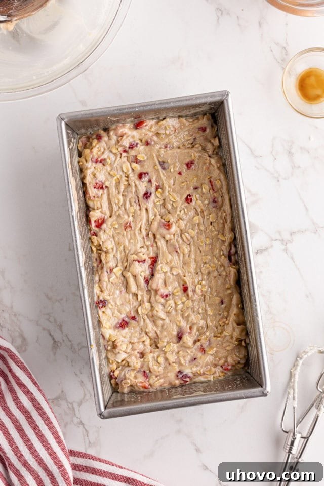 Overhead view of the swirled strawberry cream cheese bread batter evenly spread in a prepared loaf pan, ready for baking.