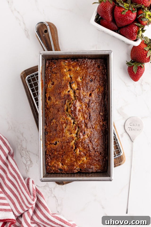 Overhead view of a freshly baked, golden-brown strawberry cream cheese bread still in its loaf pan, showing a beautiful crack down the middle.
