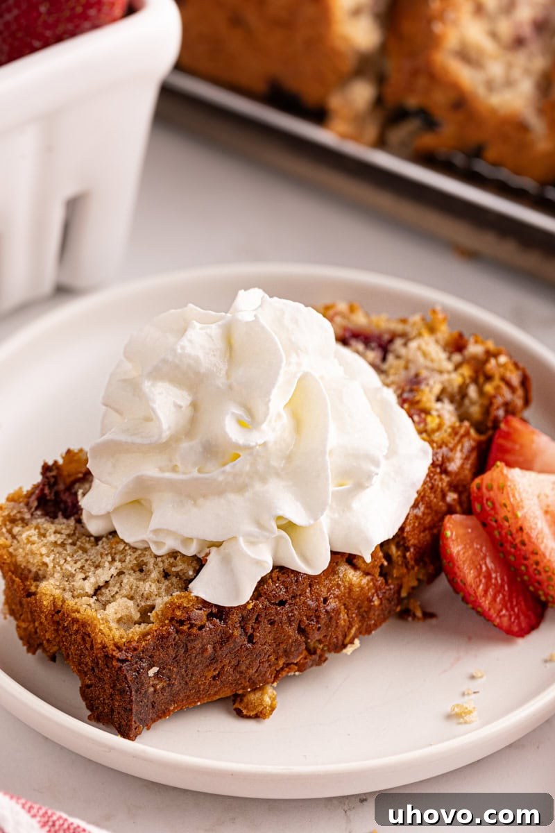 A delectable slice of Strawberry Cream Cheese Bread elegantly topped with a swirl of light, fluffy whipped cream, highlighting its dessert potential.