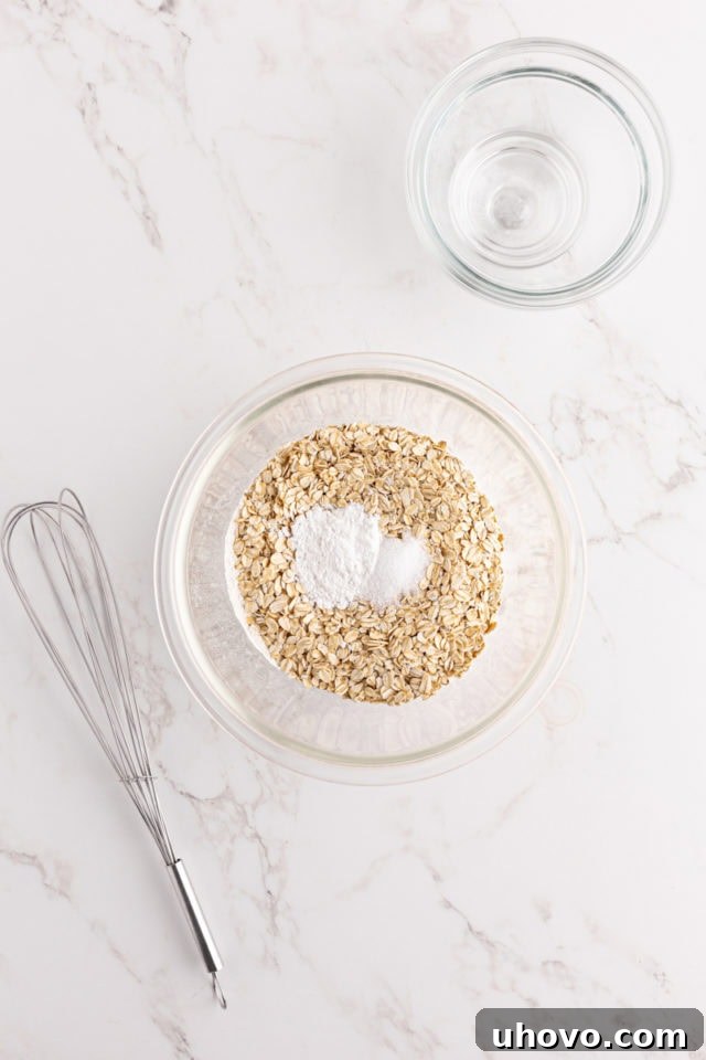 Overhead view of a mixing bowl containing flour, oats, baking powder, and salt, ready to be whisked for the strawberry quick bread.