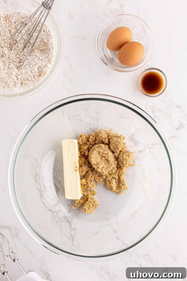 Close-up, overhead view of softened butter and light brown sugar being creamed together in a clear glass mixing bowl, showcasing the rich texture.