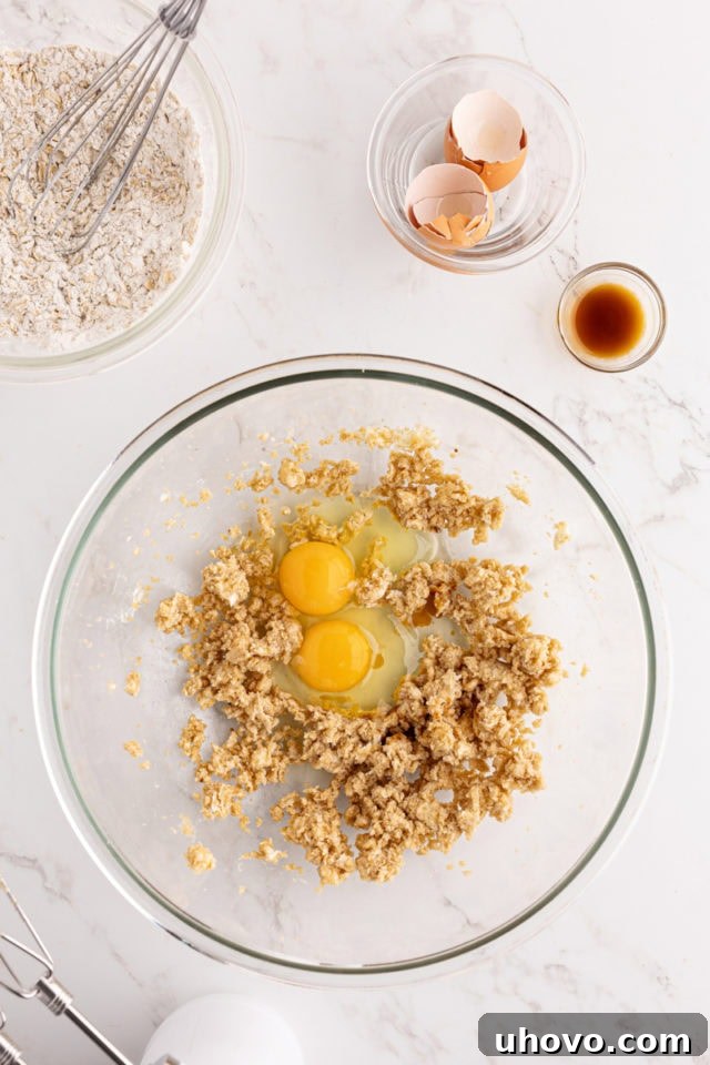 Overhead view of eggs and vanilla extract being added to the creamed butter and brown sugar mixture in a glass bowl, ready for the next mixing stage.