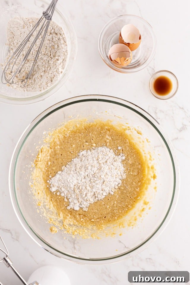 Overhead view of the dry flour and oat mixture being gradually added to the wet ingredients in a mixing bowl for the strawberry cream cheese bread batter.