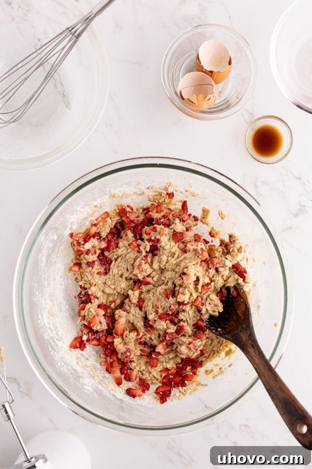 A glass mixing bowl holds the completed strawberry quick bread batter, showcasing the dispersed strawberries before the cream cheese swirl is added.