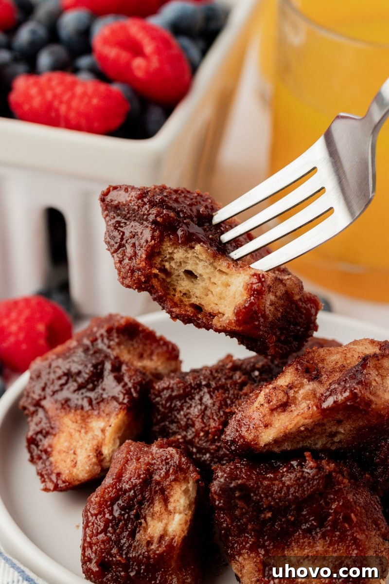 A fork lifts a sticky, chocolate-coated piece of monkey bread from a plate, highlighting the tender texture and delicious glaze.