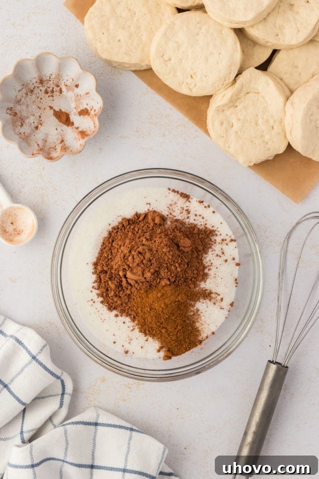 Overhead view of granulated sugar, unsweetened cocoa powder, and ground cinnamon in a clear glass bowl, before being whisked together to create the coating mixture for the chocolate monkey bread.