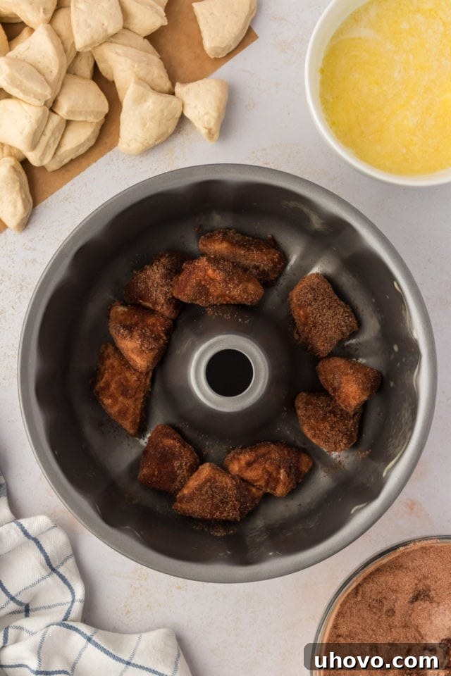 Overhead view of the first few coated biscuit dough pieces carefully arranged in the bottom of a greased Bundt pan, forming the initial layer of chocolate monkey bread.