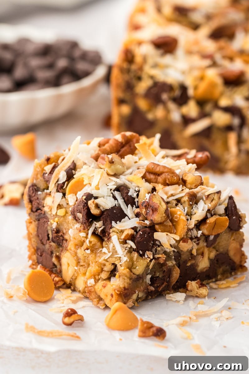 A perfectly portioned toffee square resting on parchment paper, with several other delicious bars blurred in the background, showcasing its rich texture and generous toppings.