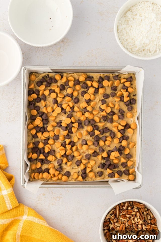 An overhead shot of a delightful scattering of chocolate chips and butterscotch chips generously sprinkled over the spread toffee squares dough in a baking pan.
