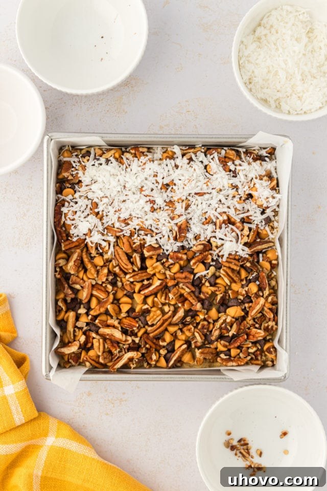 An overhead view showcasing the final toppings—crunchy pecans and sweet coconut—evenly distributed over the toffee squares dough in a baking pan.