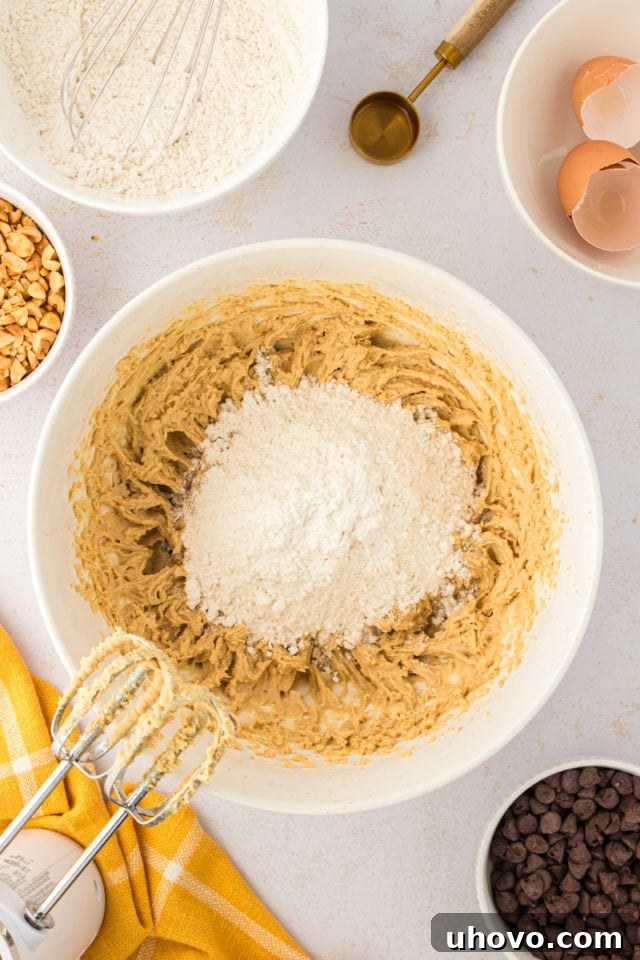 An overhead perspective of the dry flour mixture being gradually added to the wet ingredients in a white mixing bowl, forming the toffee squares dough.