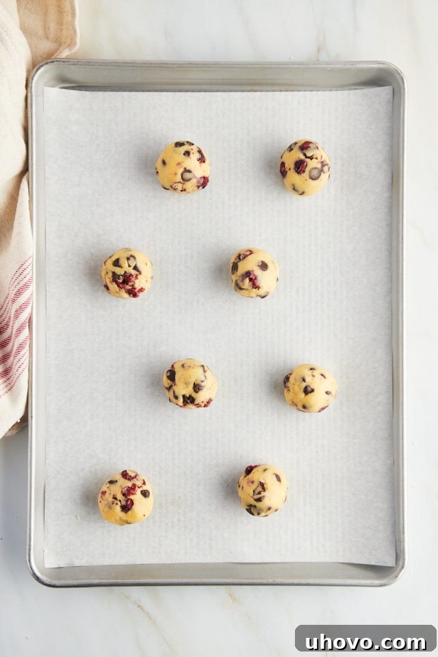 Uniform balls of cherry chocolate chip cookie dough neatly placed on a parchment-lined baking sheet, spaced apart.