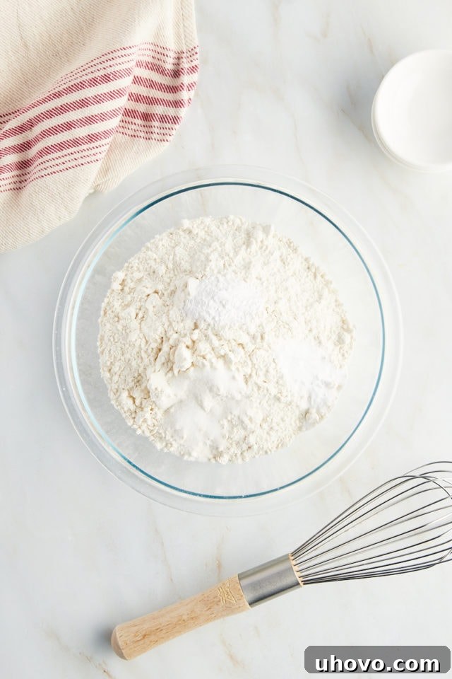 A close-up shot of flour, baking soda, and baking powder measured in a mixing bowl, ready to be combined.