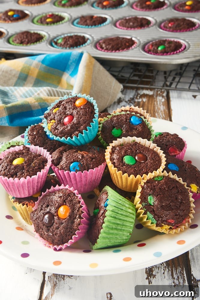 a pile of M&M Brownie Bites on a plate with more brownies in a pan in the background