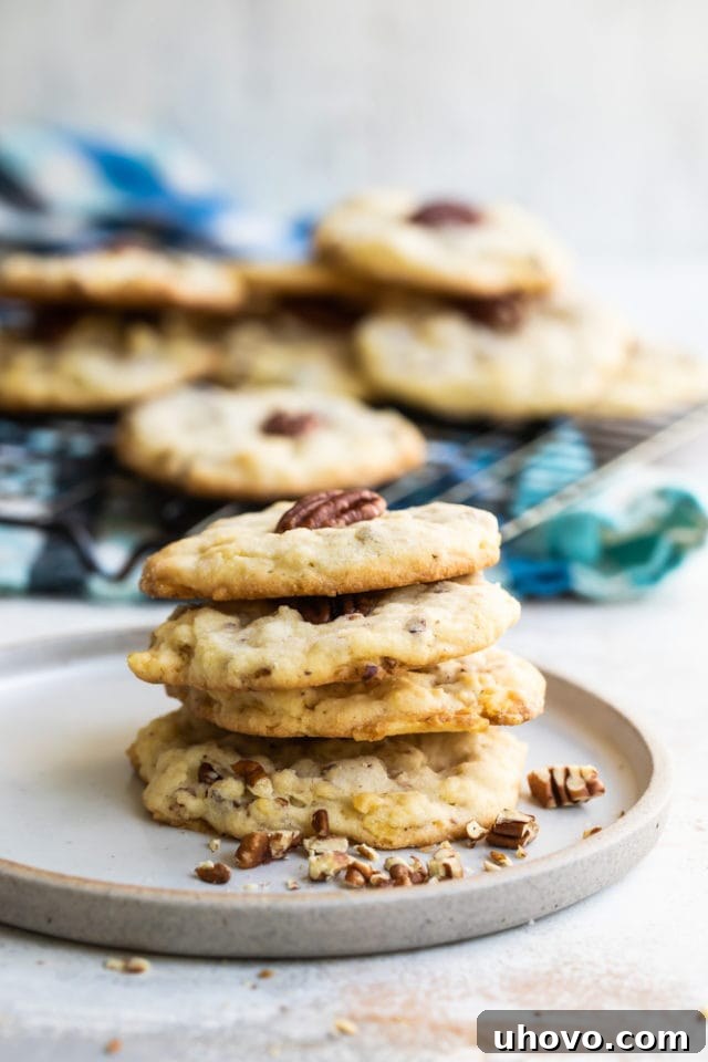 A stack of golden brown Potato Chip Cookies with visible potato chip pieces and a pecan half on top, resting on a white plate.