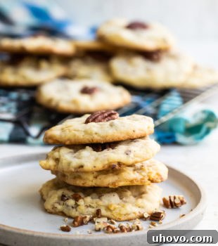 A stack of Potato Chip Cookies on a white plate, garnished with pecan halves and visible potato chip pieces.