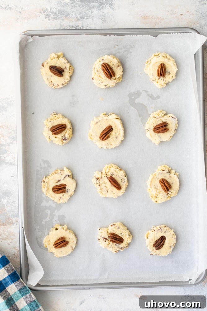 Overhead view of unbaked Potato Chip Cookie dough balls flattened and topped with pecan halves on a baking sheet, ready for the oven.