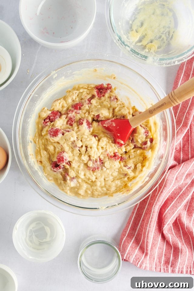 Raspberry oat muffin batter in a glass mixing bowl with raspberries gently folded in.