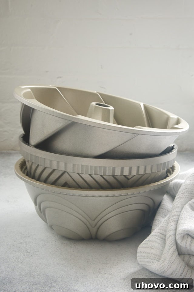Stack of shiny Bundt pans on a grey surface, illustrating variety in baking pan shapes and materials