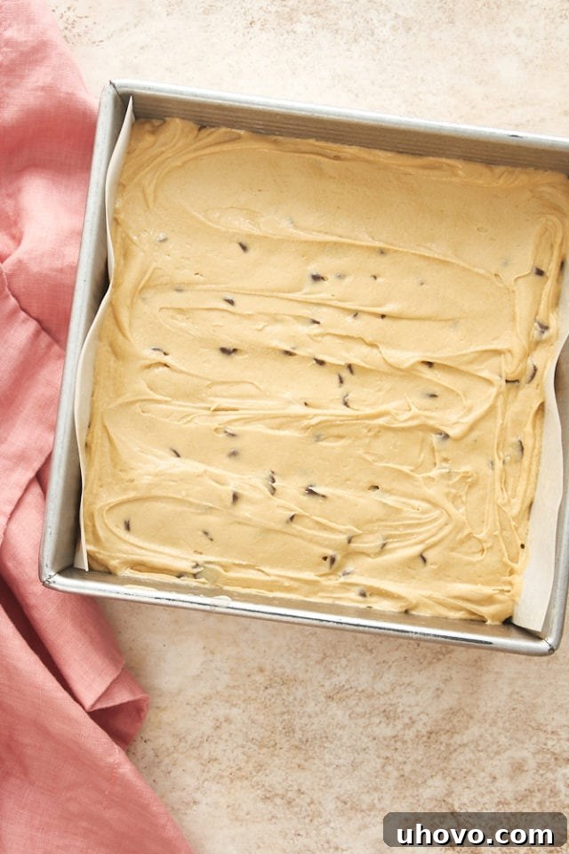 Smooth batter for Chocolate Chip Cookie Butter Snack Cake, studded with chocolate chips, spread evenly in a parchment-lined baking pan, ready for the oven.