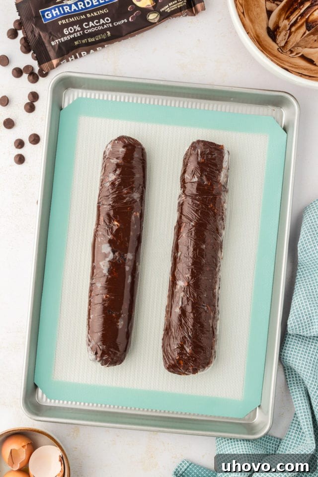 A pristine overhead shot of two perfectly formed double chocolate cookie dough logs, securely wrapped in plastic and ready for chilling.