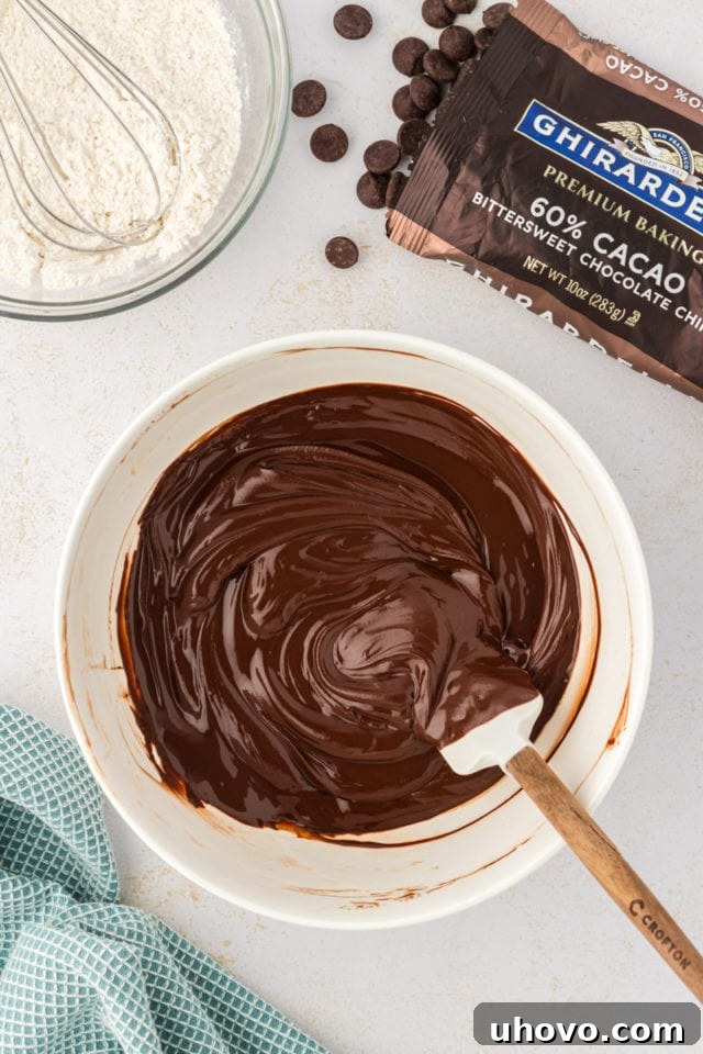 A close-up, overhead view of perfectly melted bittersweet chocolate and butter, now a smooth, glossy mixture ready to infuse the cookie dough with rich flavor.