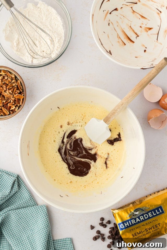 A stunning overhead view as the rich, melted chocolate mixture is carefully added to the bowl containing the beaten wet ingredients for the cookies.