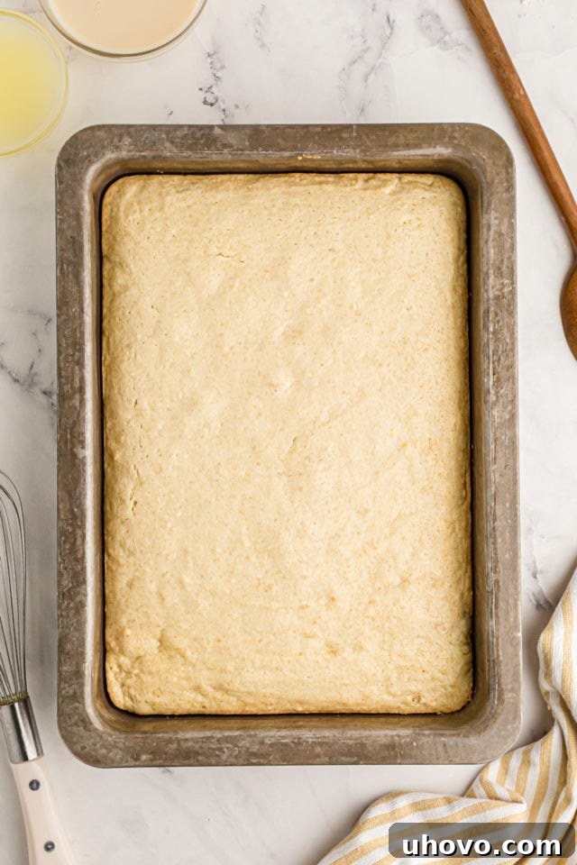 An inviting overhead view of a freshly baked, warm yellow cake resting in its pan, ready for the signature poking process to begin.