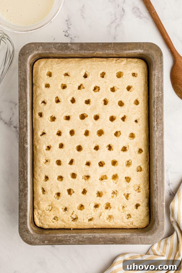 A detailed overhead shot showing numerous holes expertly poked across the surface of the warm cake, preparing it to absorb the luscious lemon filling.