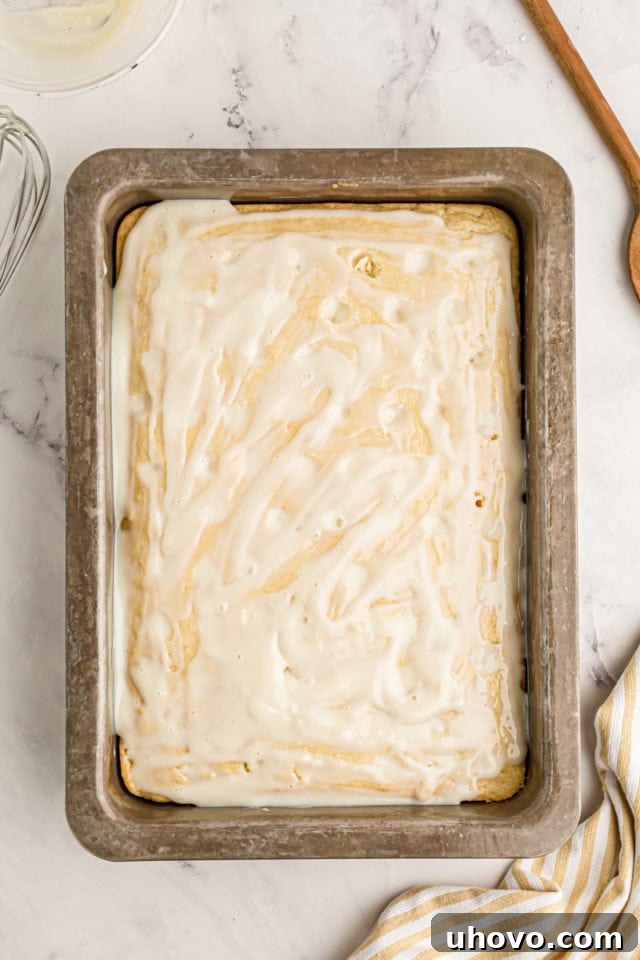 An overhead view of the lemon poke cake after the zesty condensed milk filling has been generously poured and spread, seeping into the freshly poked holes.