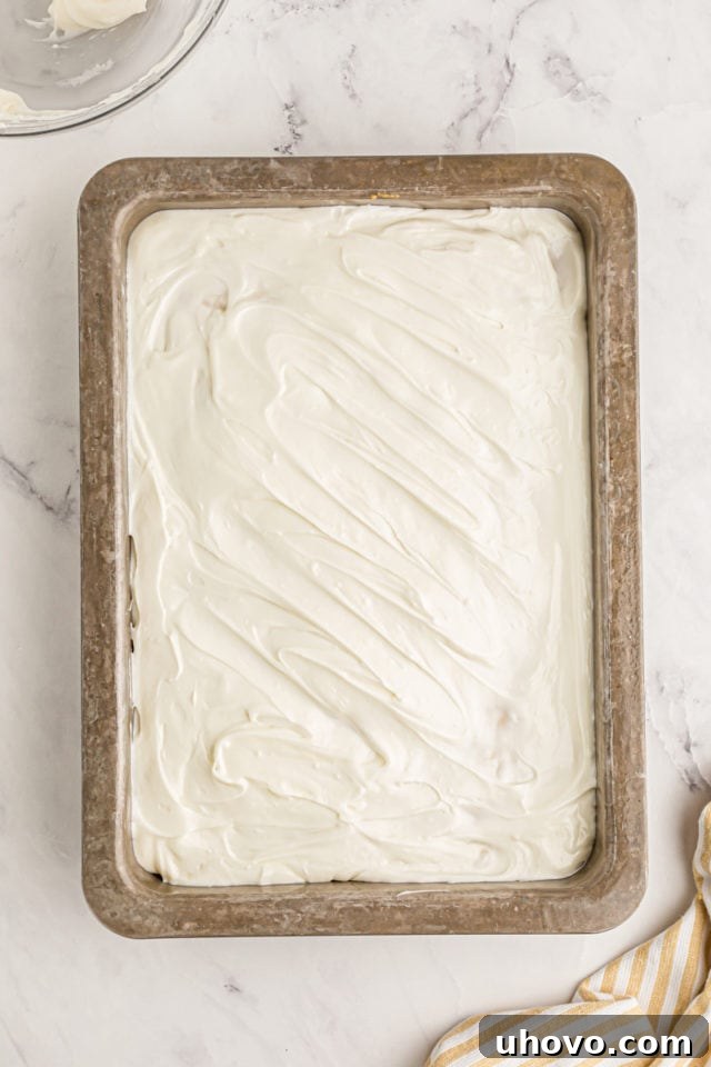 An overhead view of the perfectly frosted lemon poke cake, showcasing a smooth layer of cream cheese frosting spread over the chilled cake in its pan.