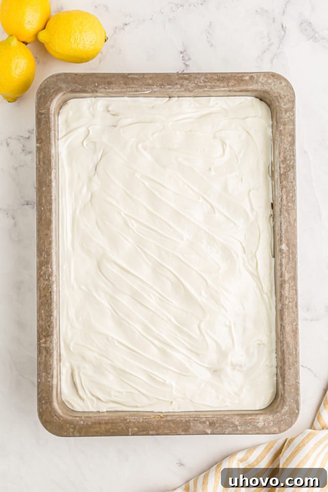 A clean overhead shot of the finished lemon poke cake in its pan, beautifully frosted and ready for slicing, tempting with its vibrant citrus appeal.