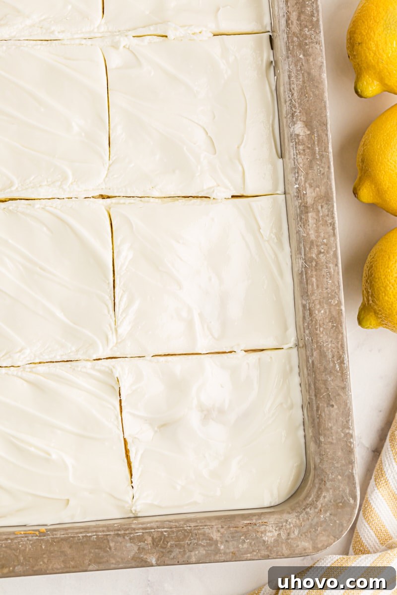 An inviting overhead view of a lemon poke cake, perfectly cut into squares within its pan, revealing its moist interior and the creamy frosting, ready to be served.