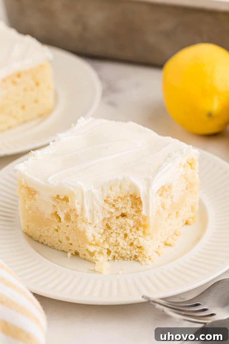 A delectable piece of lemon poke cake on a white plate, with a corner playfully eaten, inviting viewers to savor its delightful taste.