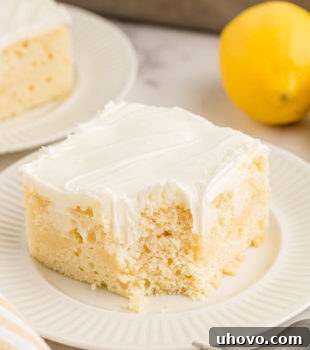 A delectable piece of lemon poke cake on a white plate, with a corner playfully eaten, inviting viewers to savor its delightful taste.