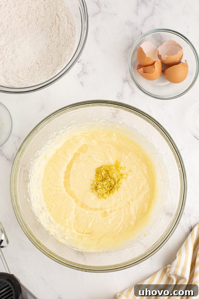 A close-up, overhead view of fresh lemon zest and juice being meticulously added to the wet ingredients in a mixing bowl, infusing the cake batter with vibrant citrus.