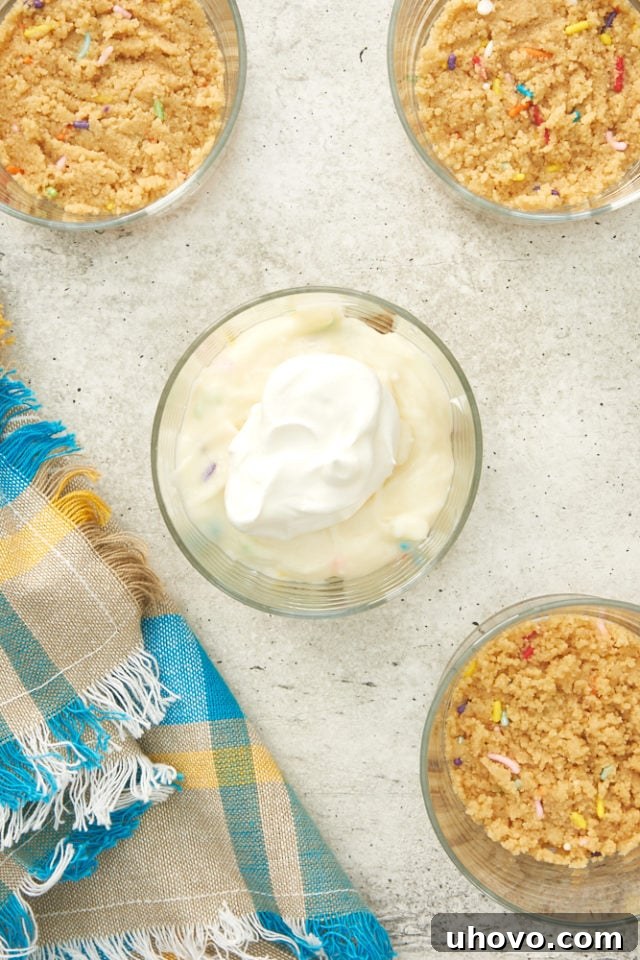 A small glass filled with cheesecake and topped with a swirl of whipped cream, awaiting final garnish.