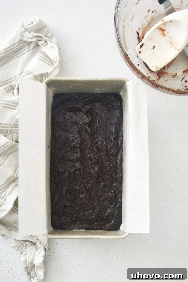 Rich brownie batter evenly spread in a parchment-lined loaf pan, ready for baking.